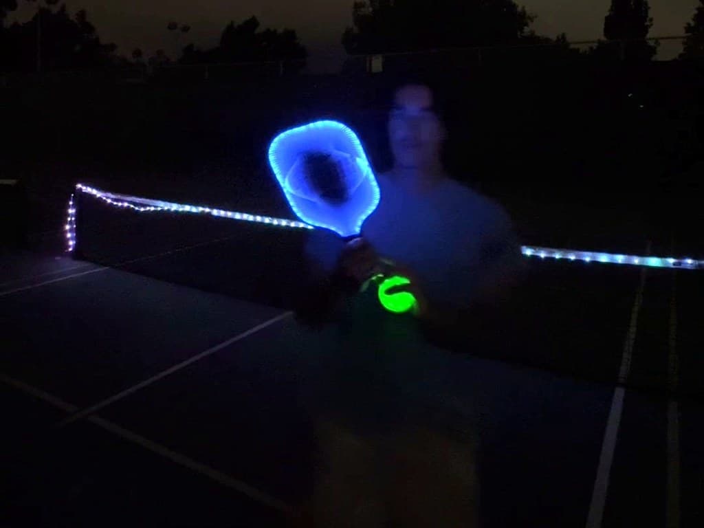 Player with a lit paddle and glow ball at a lit net, at night